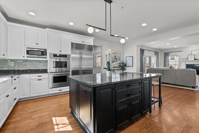 kitchen with light wood finished floors, built in appliances, a breakfast bar area, and dark cabinets