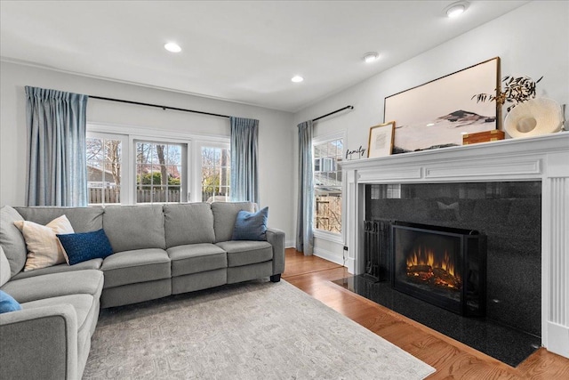 living room featuring recessed lighting, baseboards, a fireplace with flush hearth, and wood finished floors
