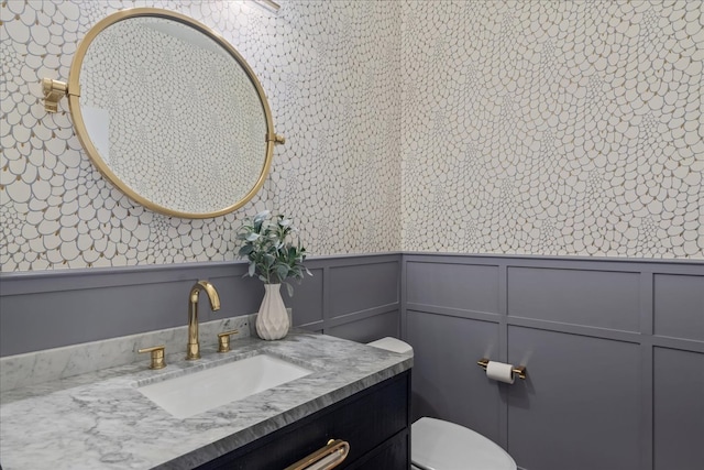 bathroom with a wainscoted wall, toilet, vanity, and a decorative wall