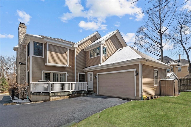 view of front facade featuring aphalt driveway, an attached garage, a chimney, and a front yard