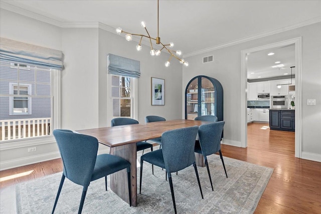 dining room featuring visible vents, baseboards, a chandelier, ornamental molding, and wood finished floors
