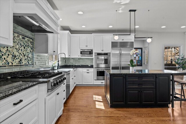 kitchen featuring light wood finished floors, built in appliances, custom exhaust hood, white cabinets, and a sink