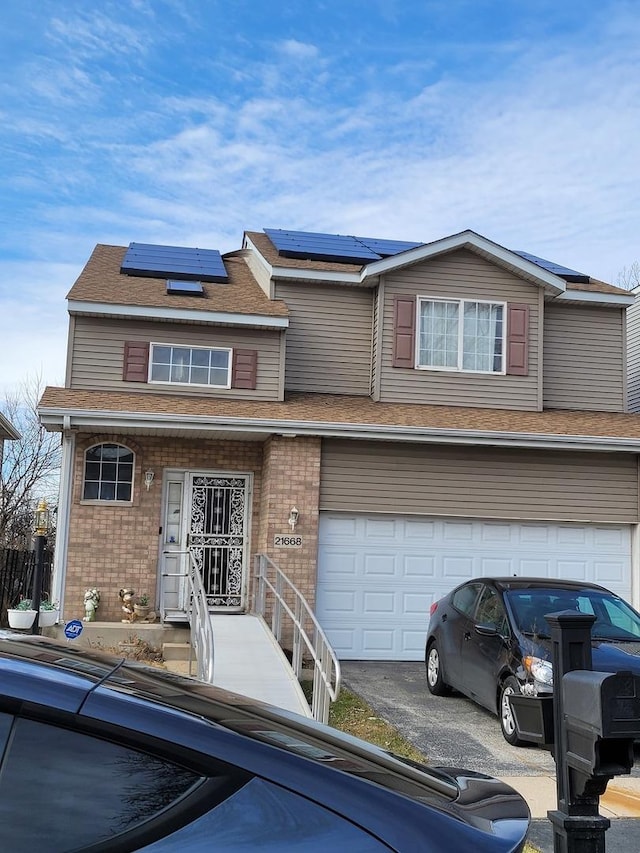 view of front of property with driveway, an attached garage, brick siding, solar panels, and a shingled roof