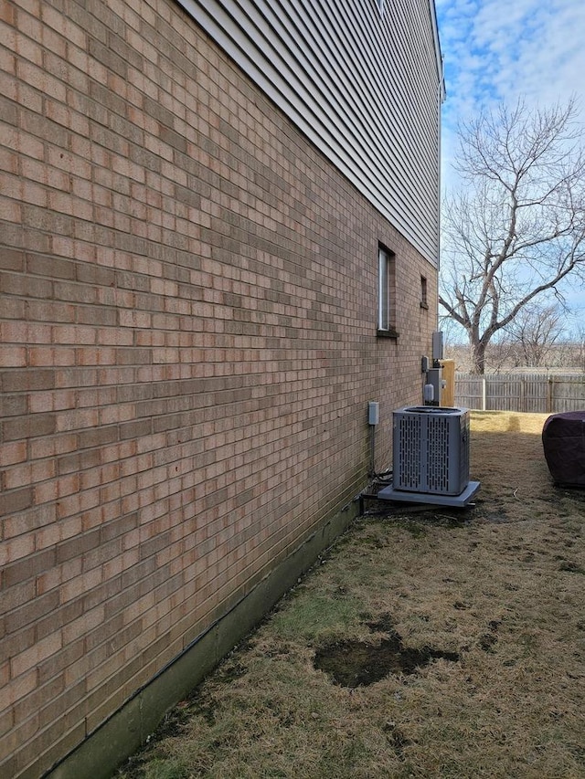 view of property exterior with central air condition unit, brick siding, and fence