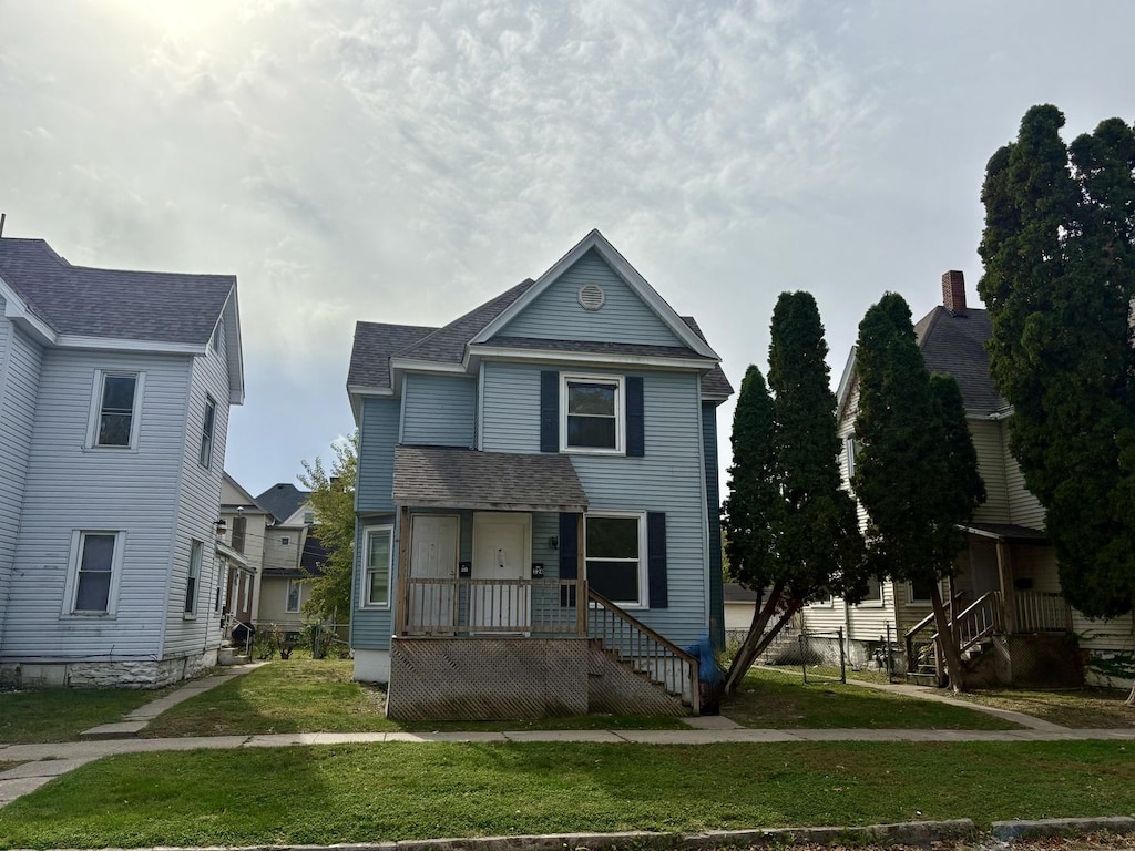 traditional-style house with a porch, a shingled roof, and a front lawn