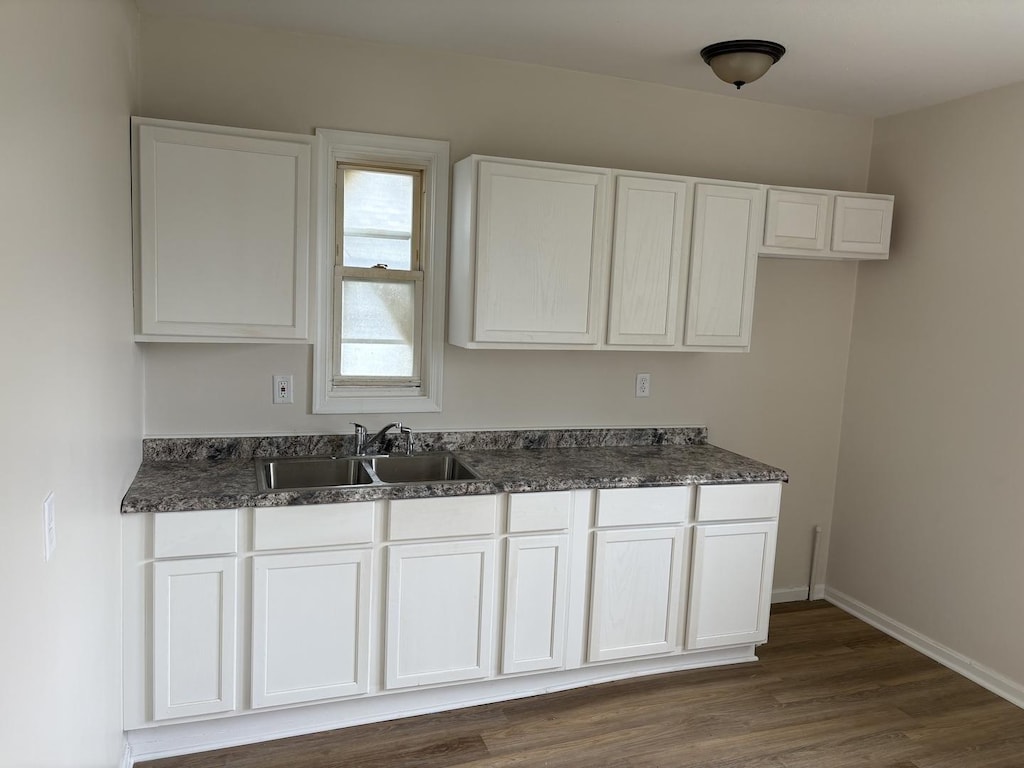 kitchen with dark wood-style flooring, white cabinets, baseboards, and a sink