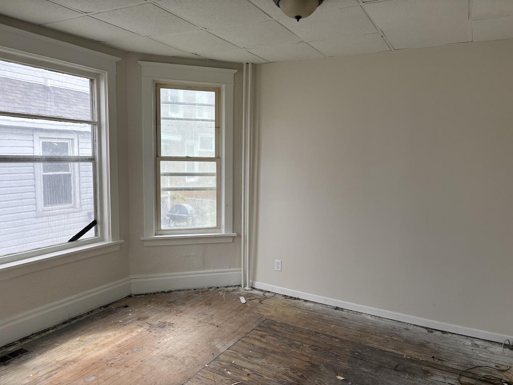 unfurnished room with a drop ceiling, baseboards, and hardwood / wood-style flooring