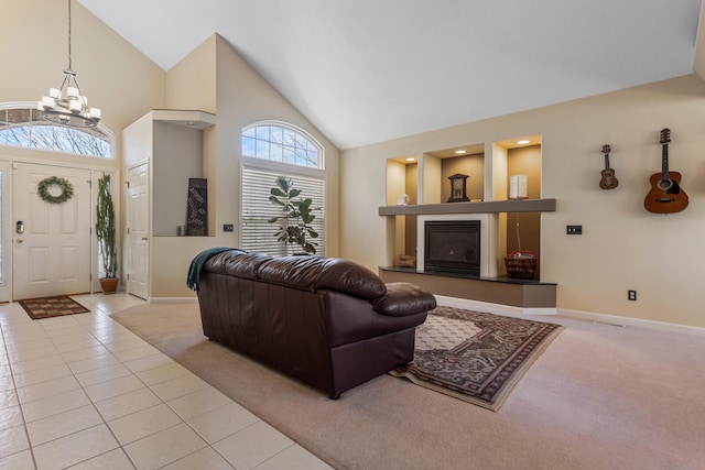 living room with a glass covered fireplace, baseboards, a chandelier, carpet flooring, and high vaulted ceiling