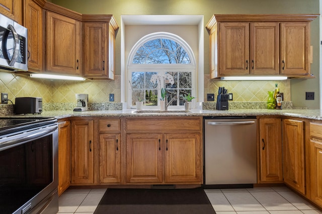kitchen featuring brown cabinets, decorative backsplash, light stone counters, and stainless steel appliances