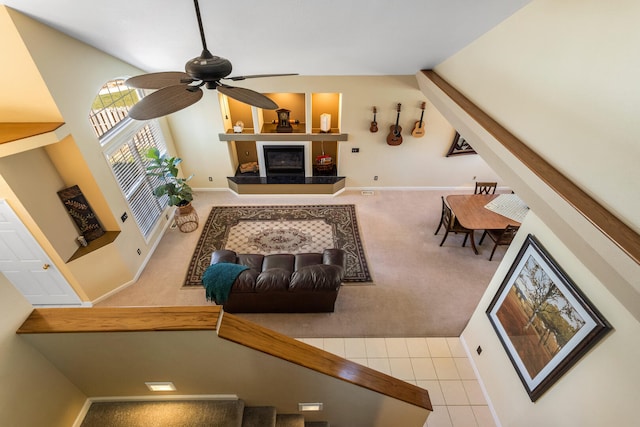 carpeted living room with ceiling fan, a glass covered fireplace, vaulted ceiling, and baseboards