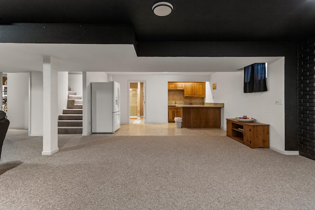 finished below grade area with baseboards, light carpet, white refrigerator with ice dispenser, stairs, and bar