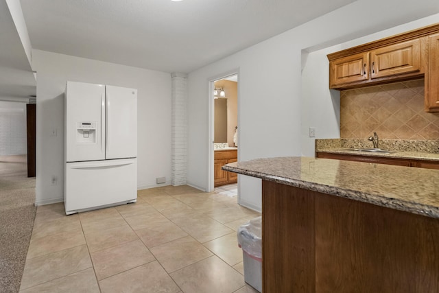 kitchen featuring tasteful backsplash, light tile patterned floors, a sink, white refrigerator with ice dispenser, and light stone counters