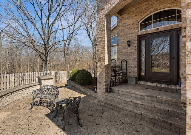 property entrance featuring a patio, brick siding, and fence