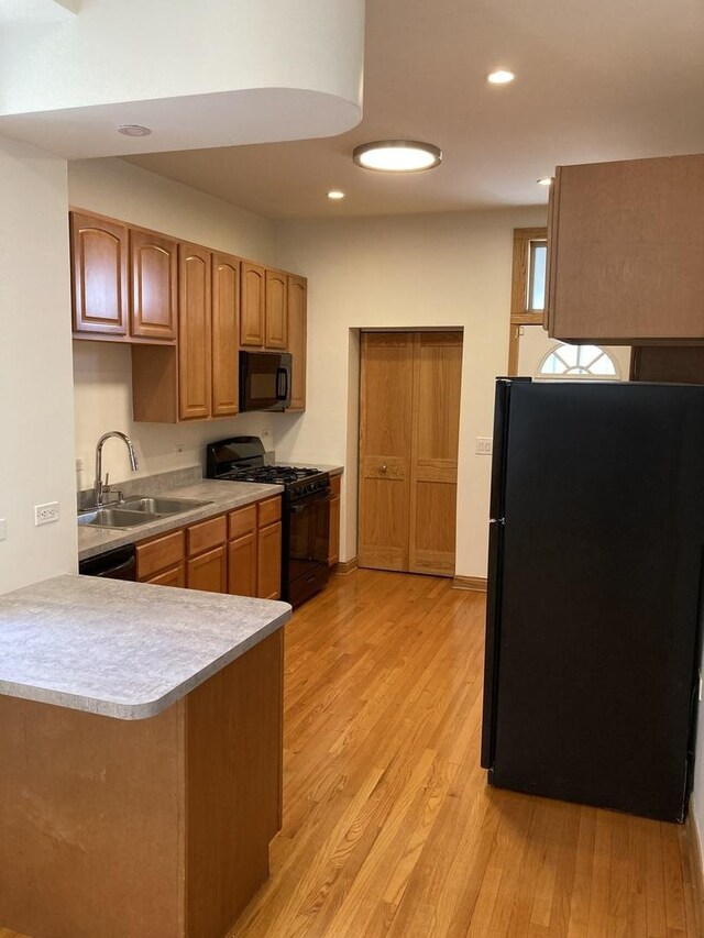 kitchen featuring black appliances, light wood-style floors, light countertops, and a sink