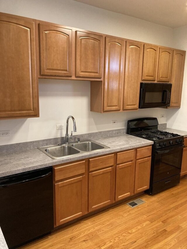 kitchen featuring visible vents, black appliances, light wood-type flooring, and a sink