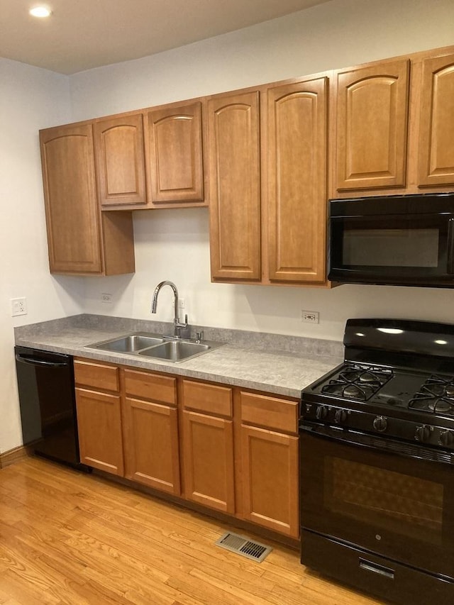 kitchen featuring visible vents, baseboards, light wood-style floors, black appliances, and a sink