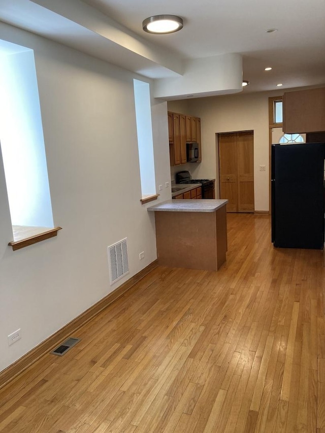 kitchen featuring black appliances, light wood-style floors, visible vents, and a peninsula