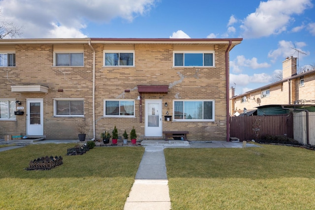 view of property with brick siding, a front yard, and fence