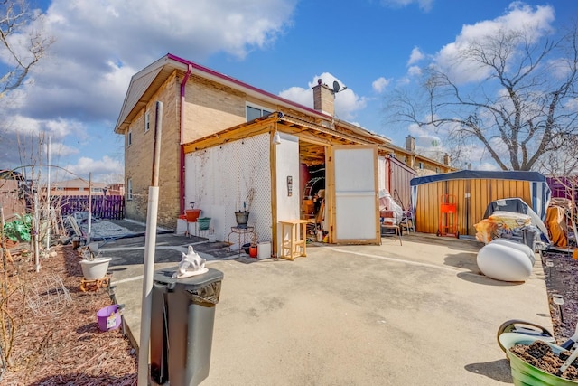 view of side of property featuring a patio, an outbuilding, fence, a chimney, and a storage shed