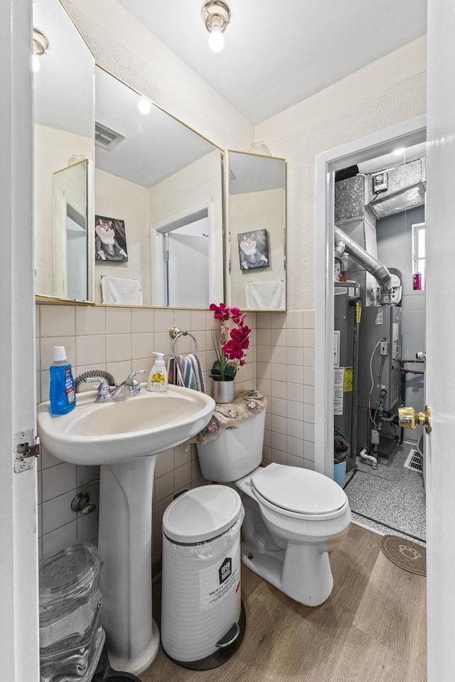 half bath featuring visible vents, toilet, wood finished floors, water heater, and tile walls