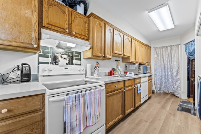 kitchen featuring light wood finished floors, under cabinet range hood, light countertops, brown cabinets, and white appliances