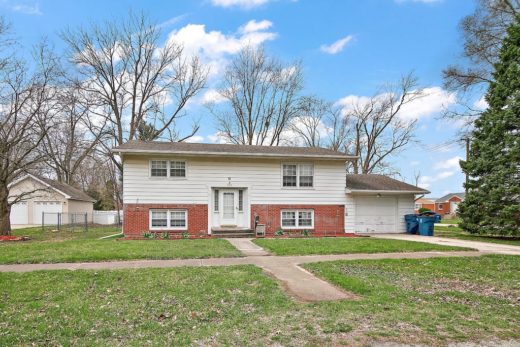 bi-level home with driveway, a front yard, fence, an attached garage, and brick siding