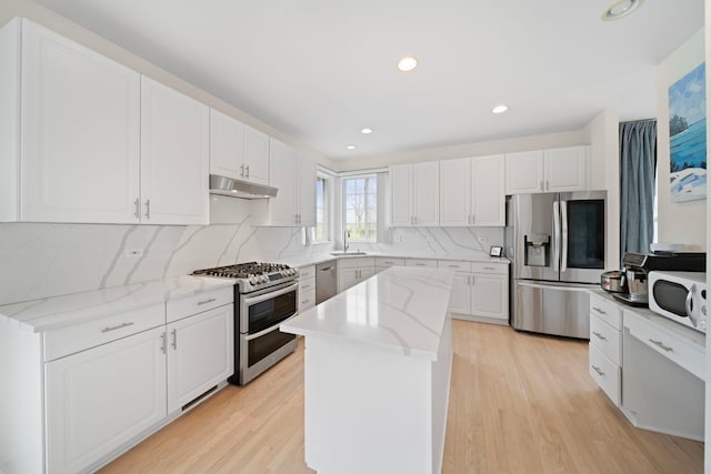 kitchen with light wood finished floors, a sink, a center island, backsplash, and appliances with stainless steel finishes
