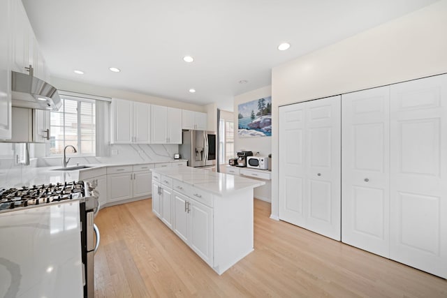 kitchen with white cabinetry, appliances with stainless steel finishes, a center island, under cabinet range hood, and light wood-type flooring