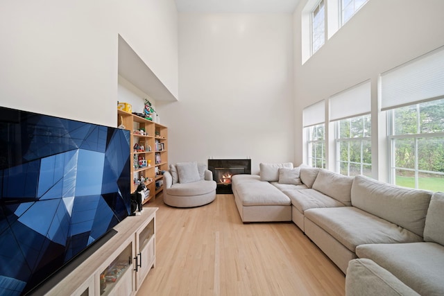 living area with a towering ceiling, plenty of natural light, light wood finished floors, and a warm lit fireplace