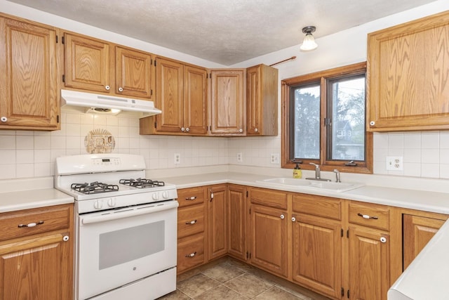 kitchen with under cabinet range hood, white gas range, light countertops, a sink, and tasteful backsplash