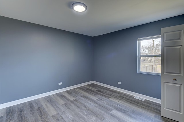 empty room featuring wood finished floors, baseboards, and visible vents