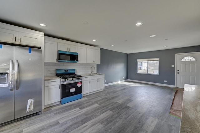kitchen featuring a sink, appliances with stainless steel finishes, light wood finished floors, decorative backsplash, and baseboards
