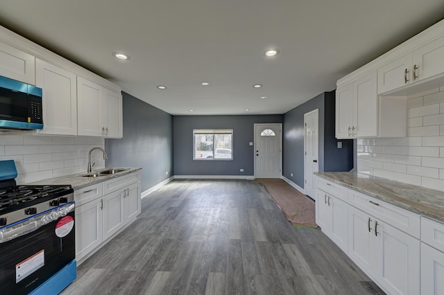 kitchen featuring wood finished floors, baseboards, a sink, stainless steel appliances, and white cabinetry
