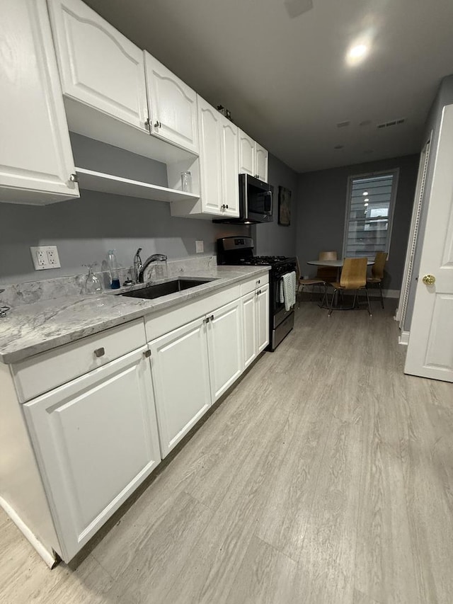 1812 W Erie St, Chicago, IL 60622 - kitchen featuring stainless steel microwave, black range with gas stovetop, light wood-style flooring, white cabinetry, and a sink