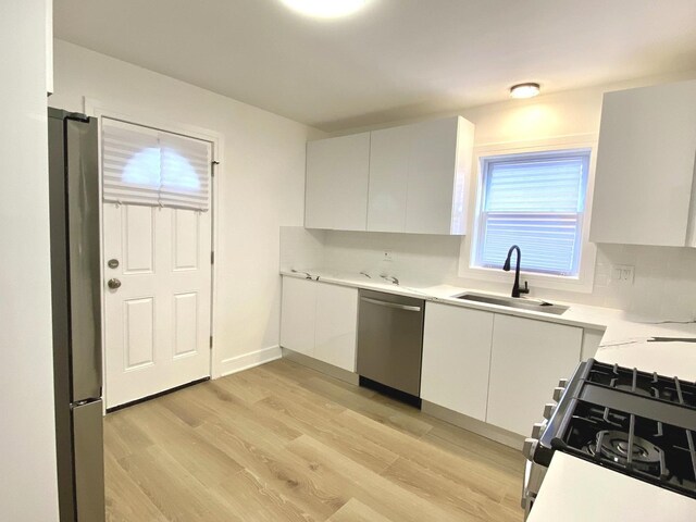 kitchen featuring light wood-style flooring, a sink, light countertops, appliances with stainless steel finishes, and white cabinetry