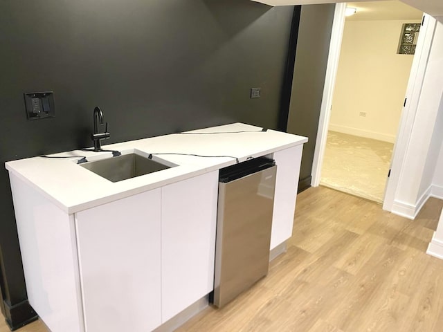 kitchen with light wood-type flooring, white cabinetry, light countertops, dishwashing machine, and baseboards