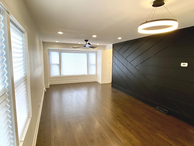 unfurnished living room with dark wood finished floors, visible vents, wood walls, and a wealth of natural light