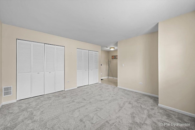 unfurnished bedroom with carpet flooring, baseboards, visible vents, and two closets