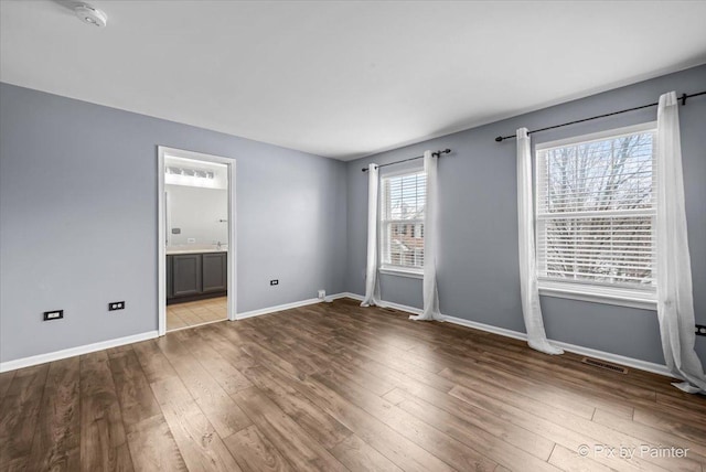 unfurnished bedroom featuring ensuite bath, wood finished floors, visible vents, and baseboards