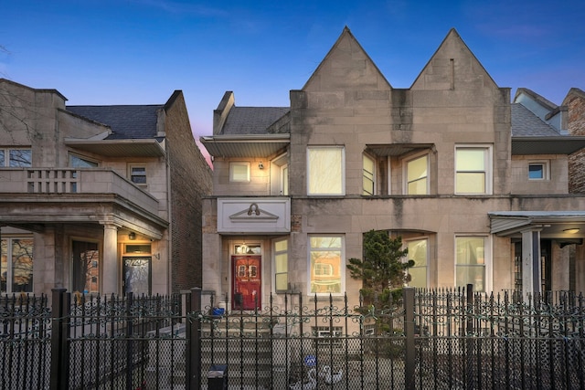multi unit property with a fenced front yard, stone siding, and a shingled roof