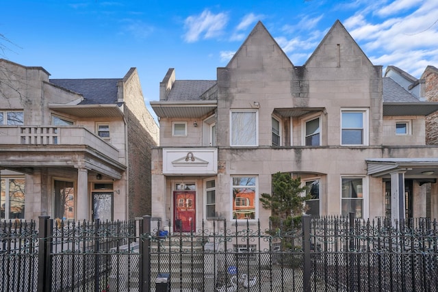 multi unit property with a fenced front yard, stone siding, and roof with shingles