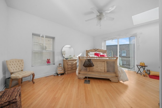 bedroom with baseboards, ceiling fan, light wood-style flooring, a skylight, and access to outside