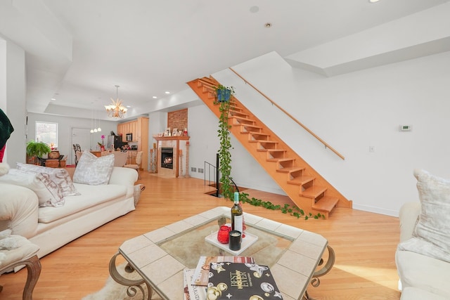 living area featuring a fireplace with flush hearth, stairs, an inviting chandelier, and wood finished floors