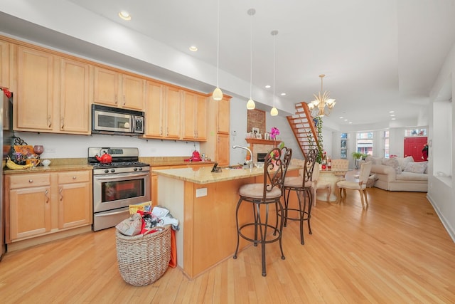 kitchen featuring light wood finished floors, light brown cabinets, appliances with stainless steel finishes, and an inviting chandelier