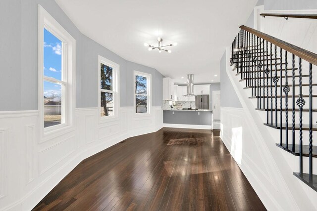 unfurnished living room with an inviting chandelier, stairway, a decorative wall, and dark wood-type flooring