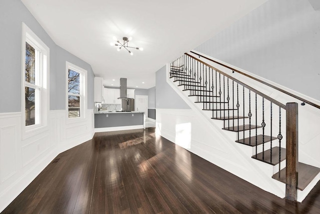 interior space featuring stairway, a decorative wall, dark wood-style flooring, and a chandelier