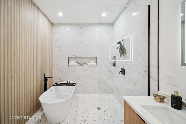 bathroom with a marble finish shower, tile walls, a freestanding bath, vanity, and recessed lighting