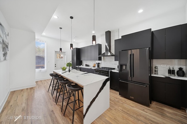kitchen with dark cabinetry, premium appliances, and wall chimney range hood