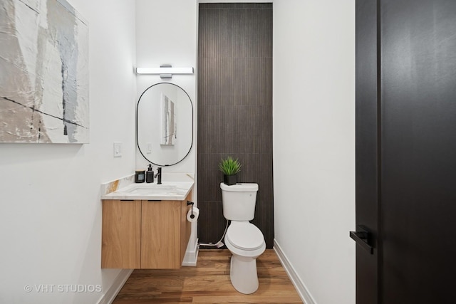 half bath featuring vanity, toilet, baseboards, and wood finished floors