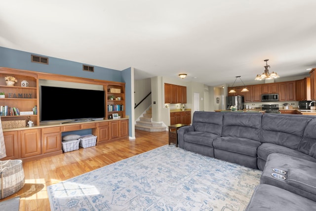 living room with an inviting chandelier, light wood-style floors, stairway, and visible vents